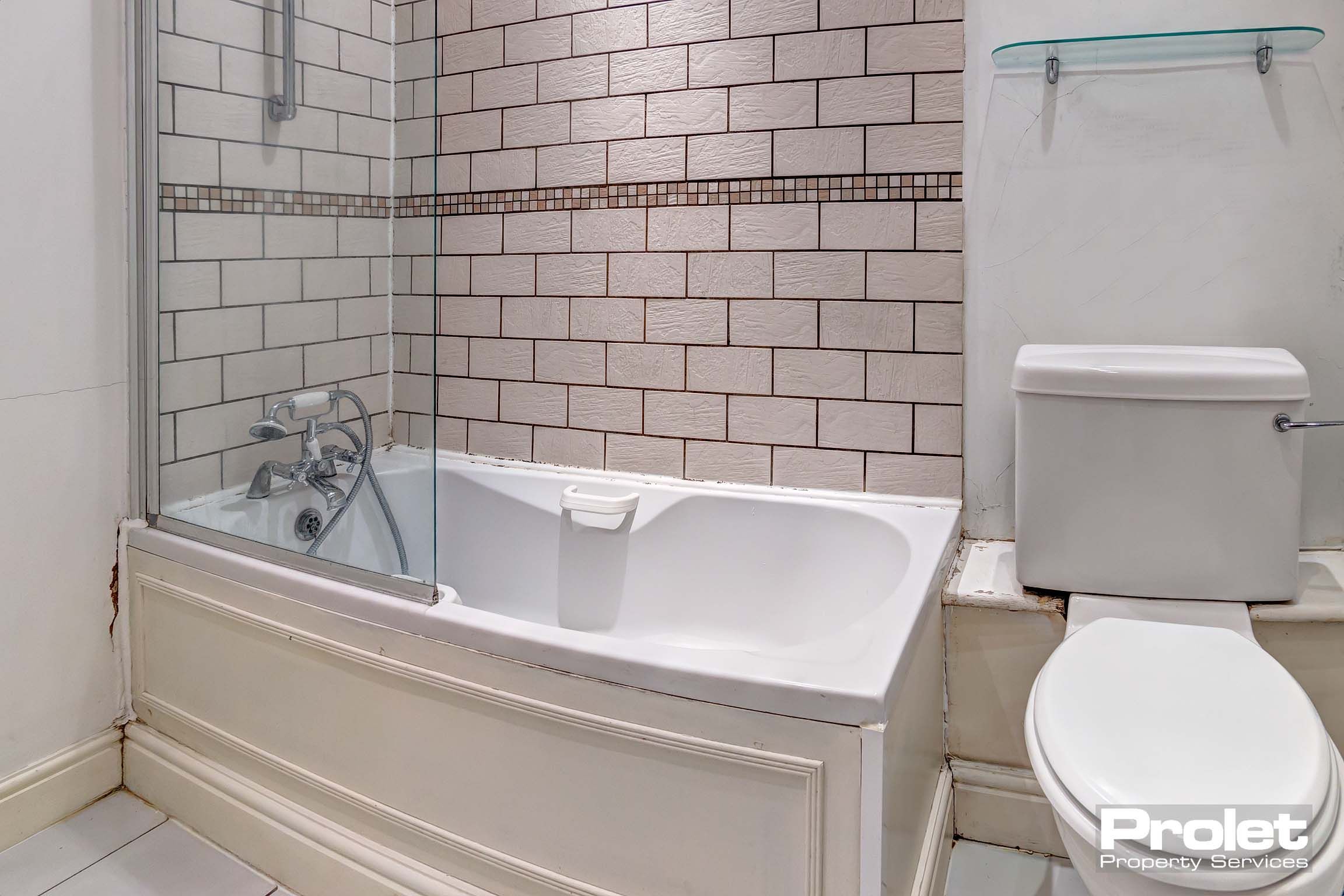 Bathroom with tiled walls, shower over bath, and toilet