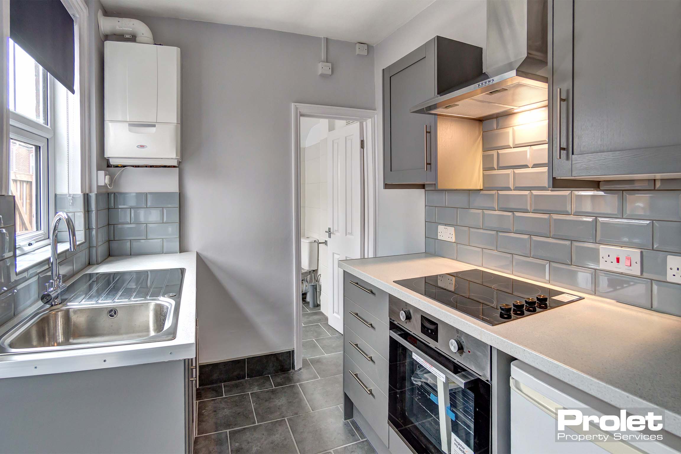 Grey kitchen with white units with oven, hob, washing machine and fridge