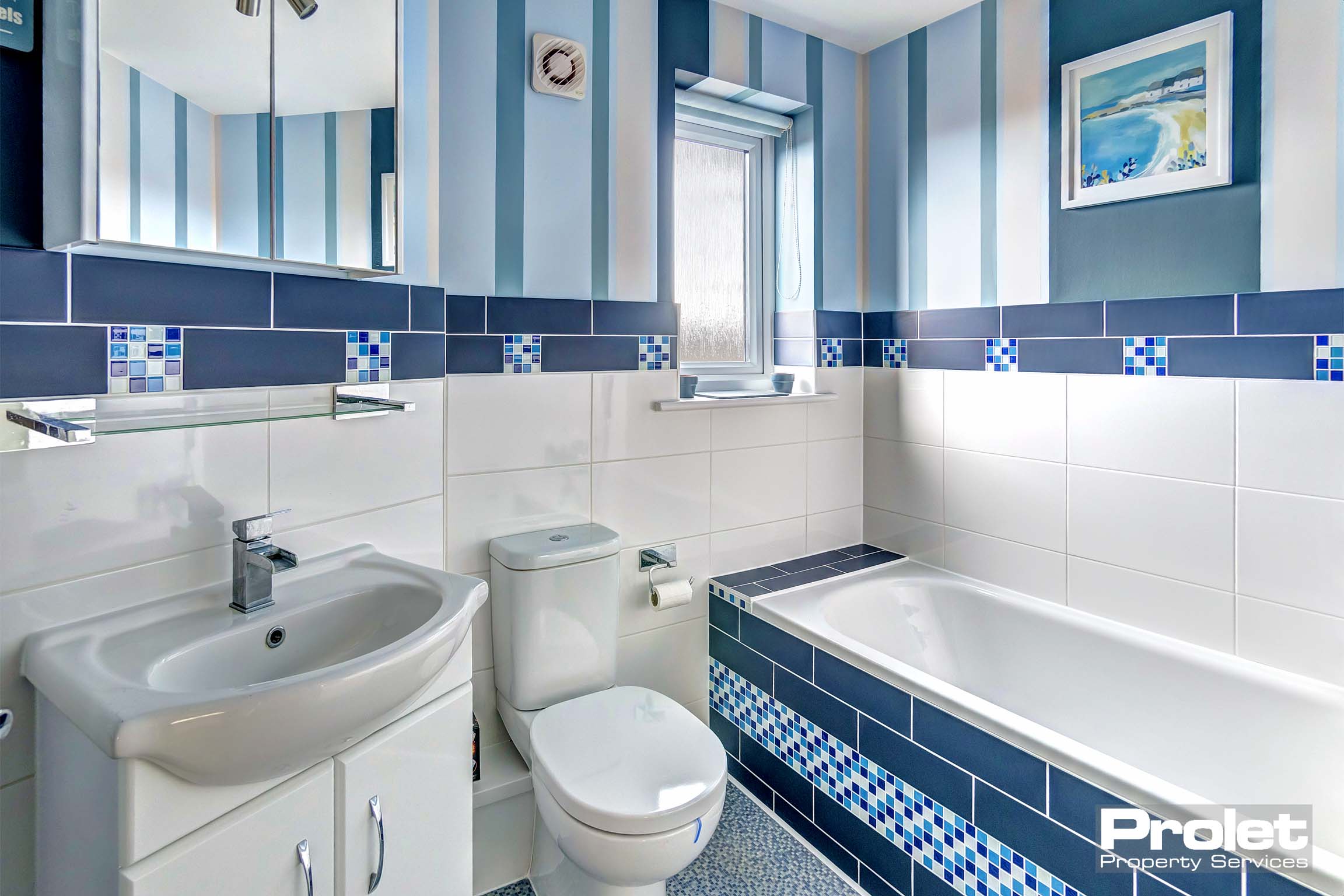 Bathroom with white suite and blue tiles. Shower off taps over sink