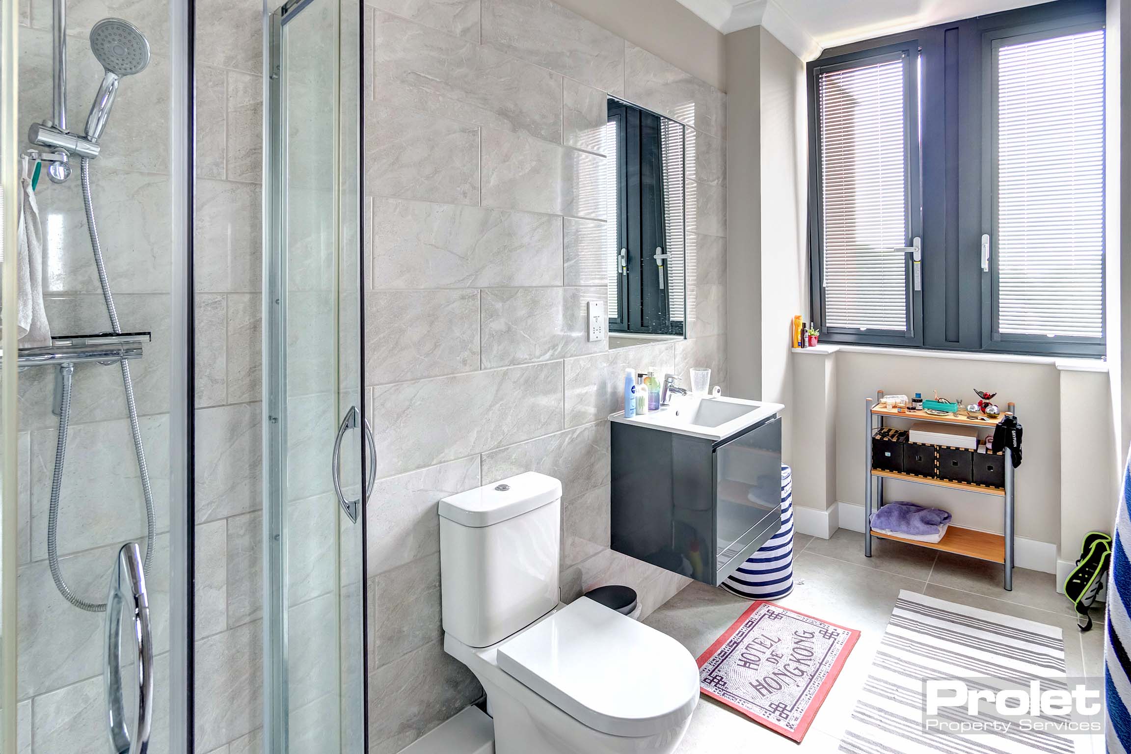 Grey tiled bathroom with shower cubicle, toilet, and sink