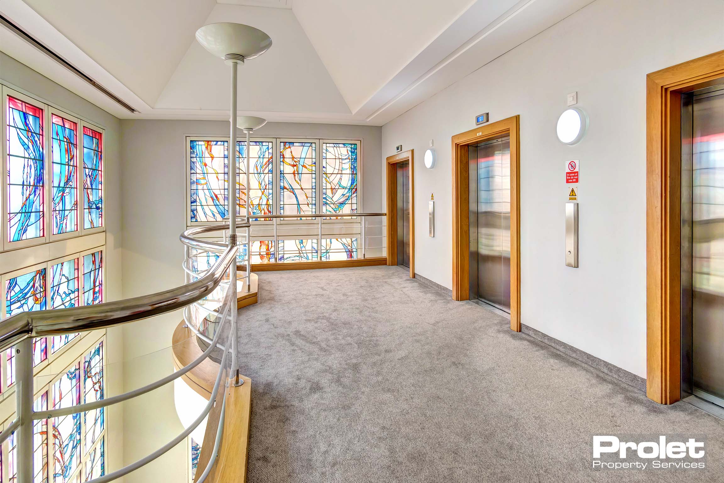 Mezzanine corridor area with lifts, and large stained glass windows.