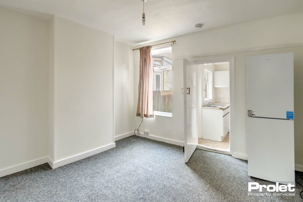 Dining room, leading to kitchen, with white walls, and fridge freezer