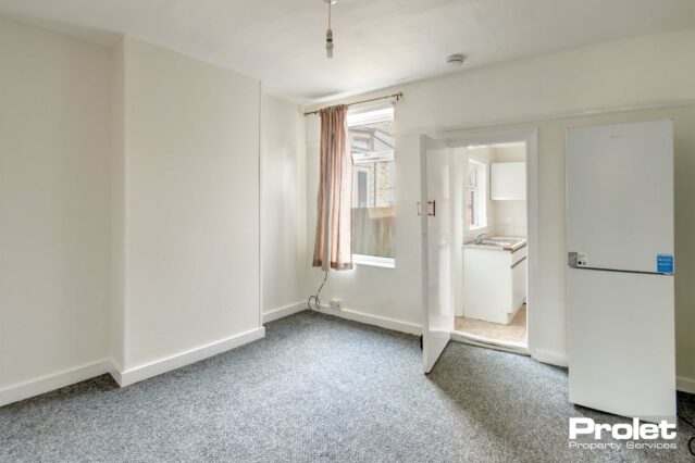 Dining room, leading to kitchen, with white walls, and fridge freezer