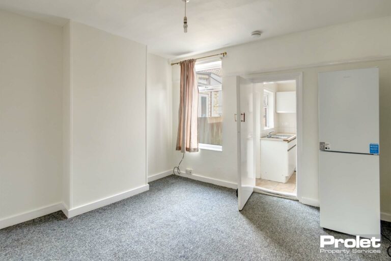 Dining room, leading to kitchen, with white walls, and fridge freezer