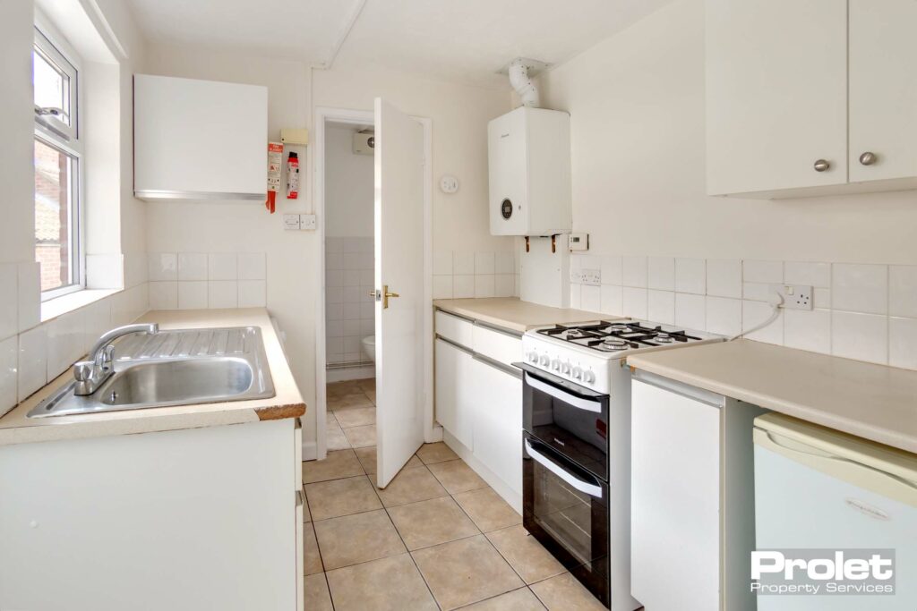 Galley style kitchen with white cabinets, under counter fridge, and gas cooker