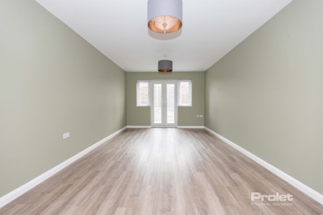 Lounge area with pale green walls, wood effect flooring, and french doors to back garden