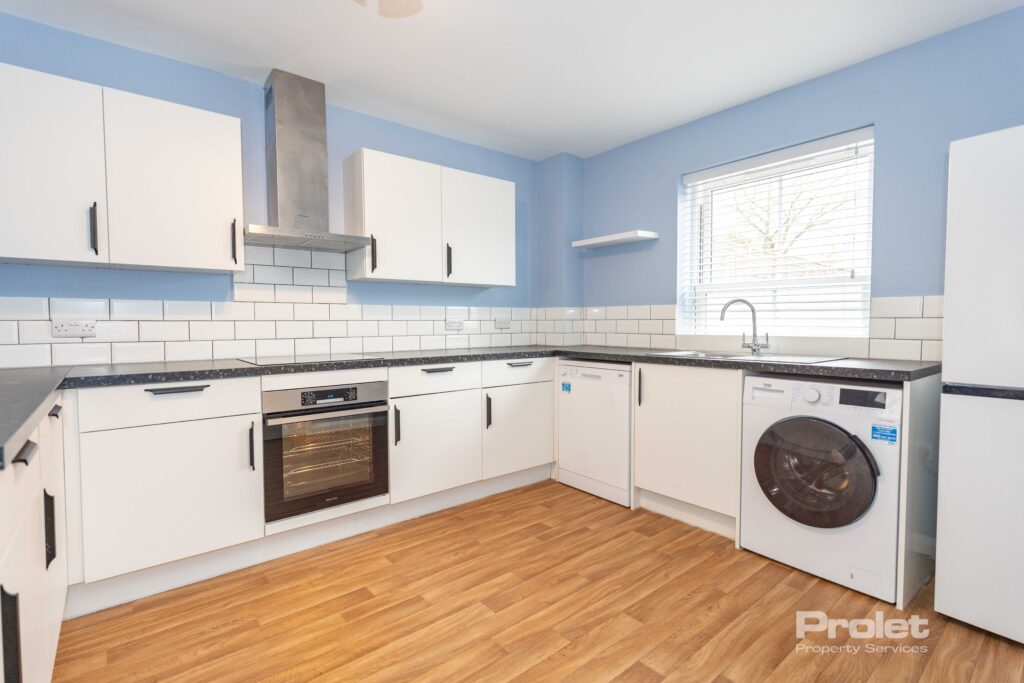Modern kitchen with white cabinets, black worktop, blue walls, and wood effect flooring. ,