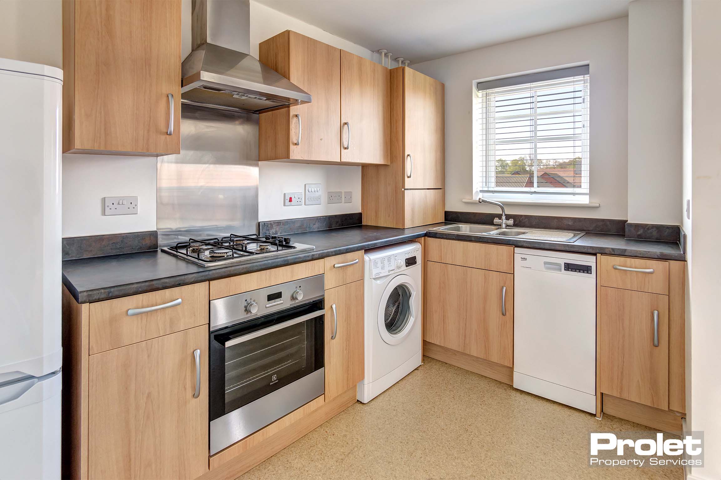 Open plan kitchen off lounge with beach effect units and black worktops. Built in oven and hob. Slimline dishwasher and washing machine