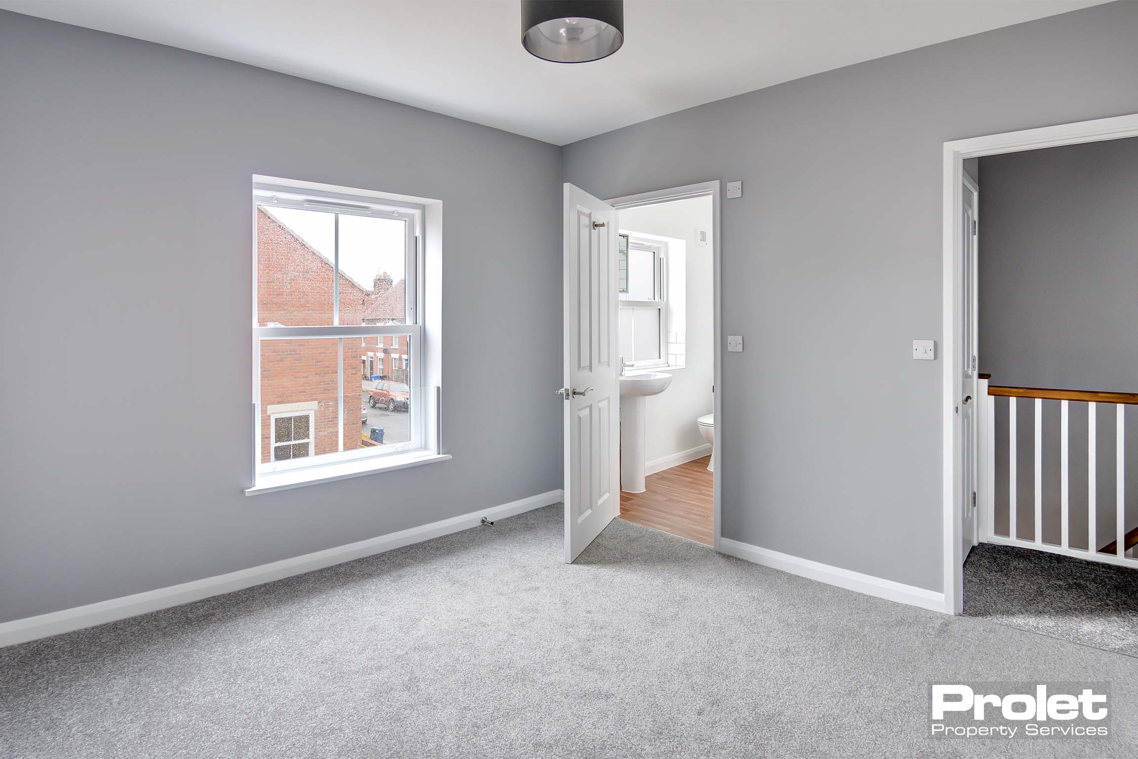 Large double bedroom with grey walls and carpet. Leads to en-suite bathroom
