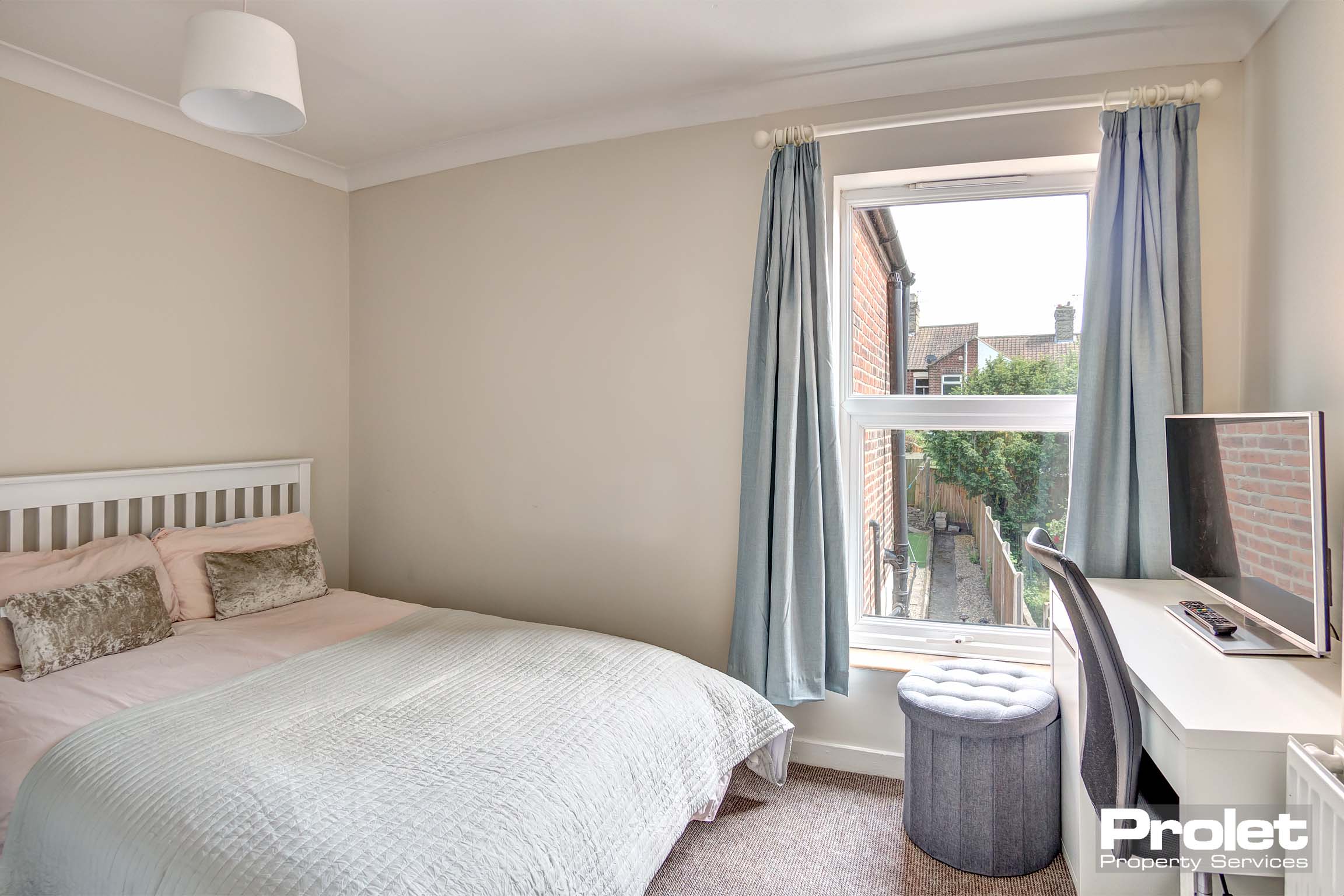 Double bedroom with a modern white desk and chair, a white wooden bedframe and some duck egg blue curtains.