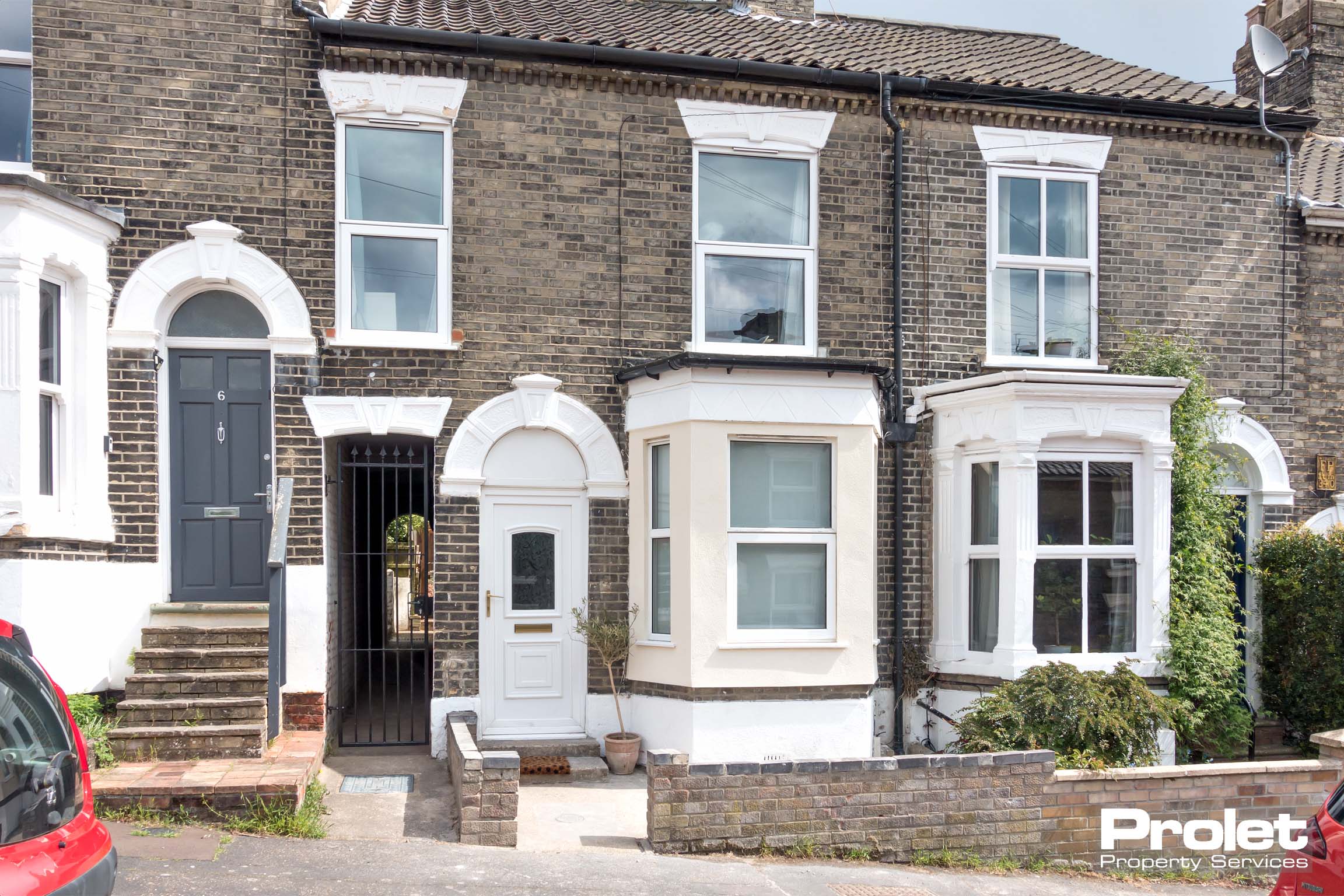 Brick terraced house with a white door and side alley to the back garden