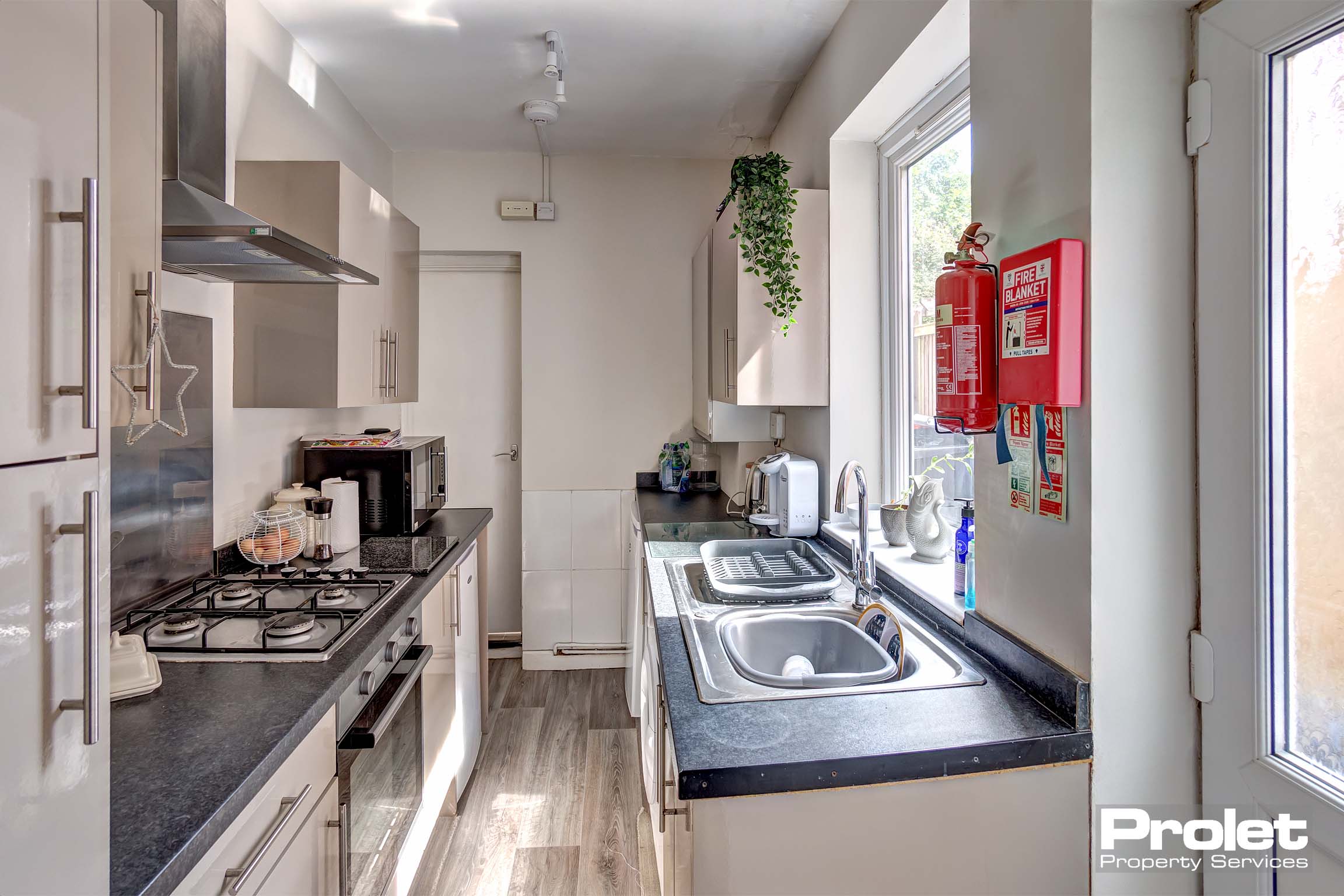 Galley style kitchen with off white units and a black worktop.