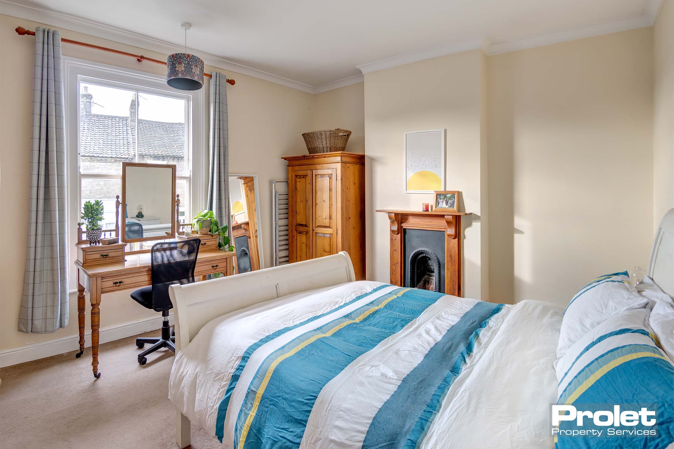 Double bedroom, with large window, cream walls, cream carpet, and period fireplace