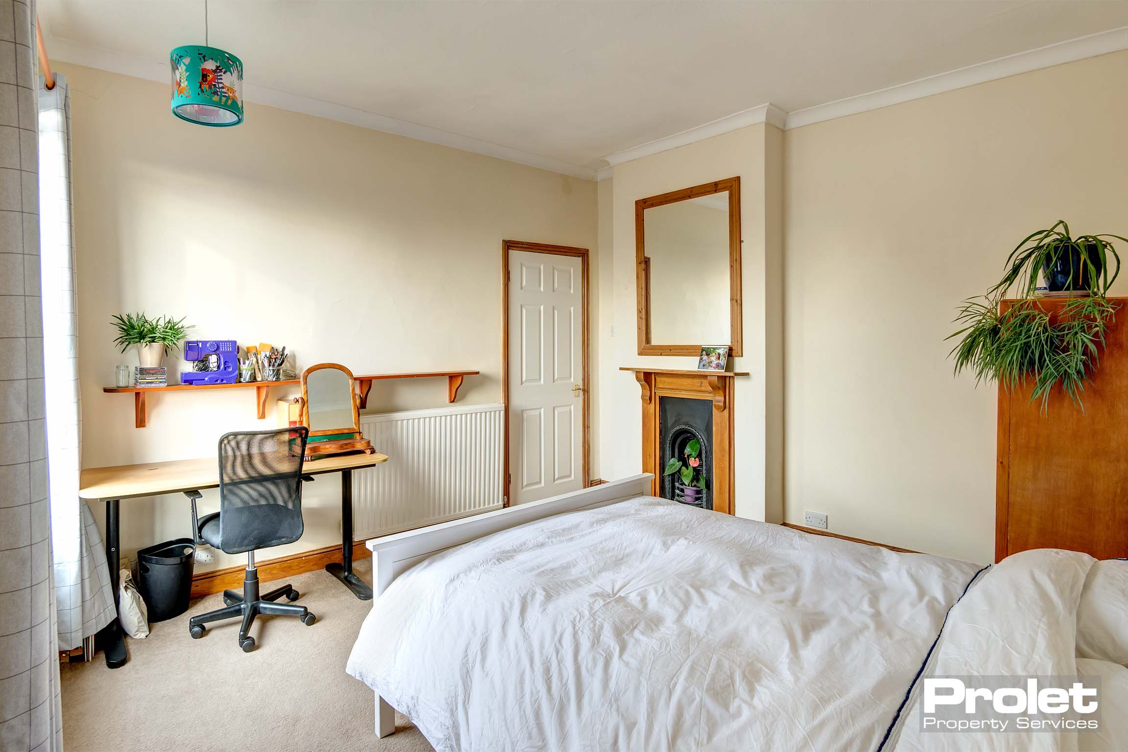 Double bedroom with cream walls, cream carpet, and period fireplace