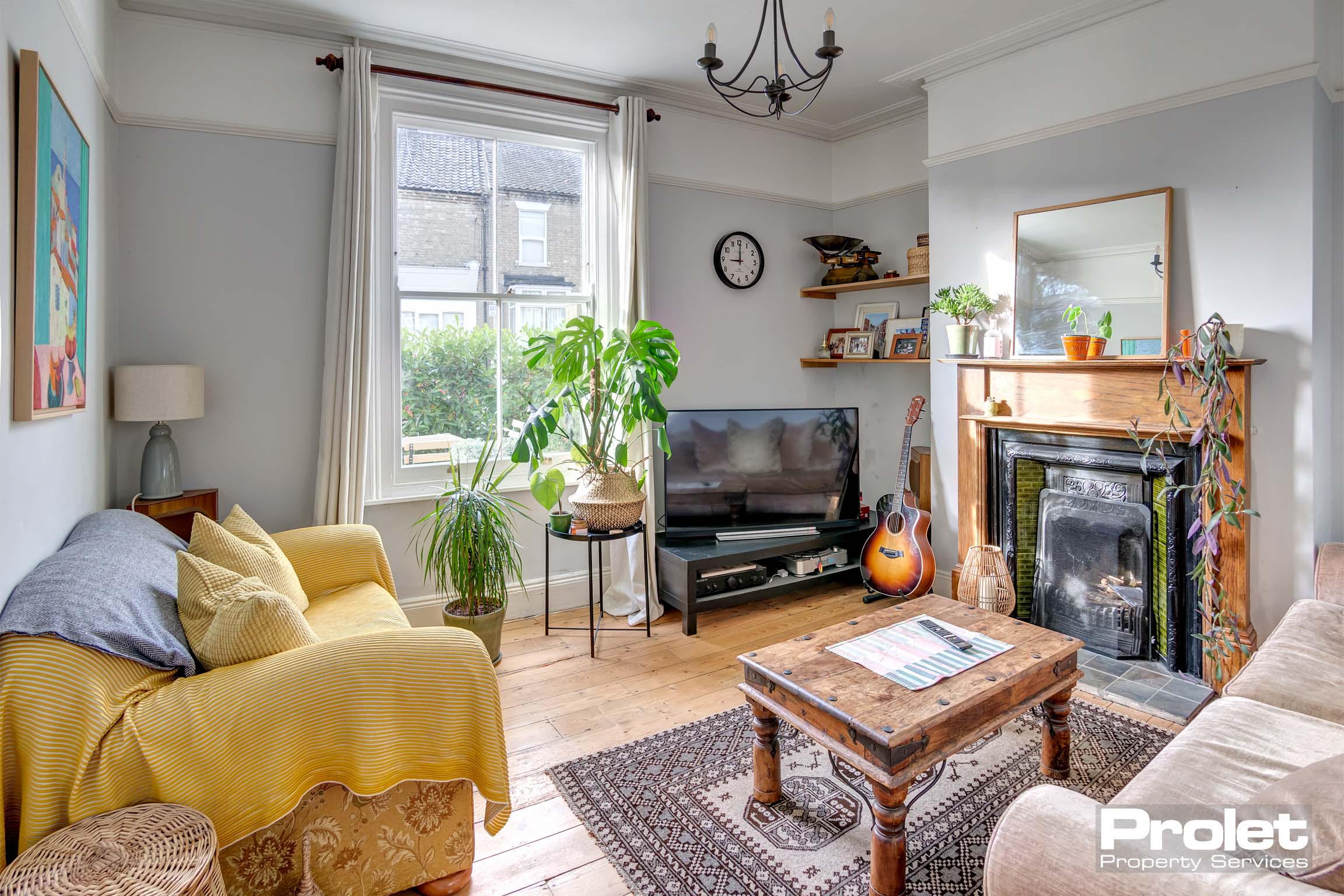 Living room with wooden floor, period fireplace, and large window.