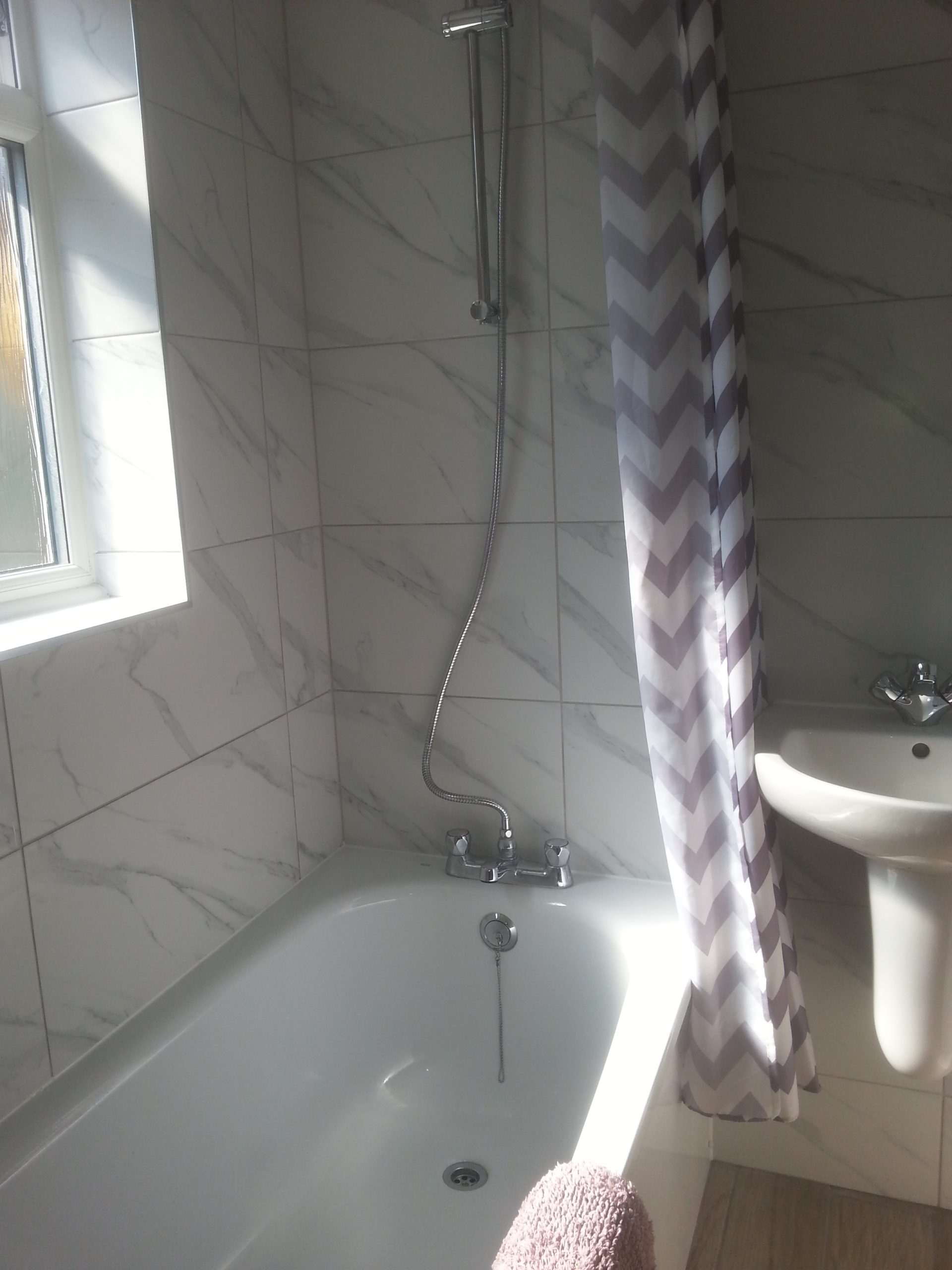 Bathroom with a white bath tub and a shower over the bath.
