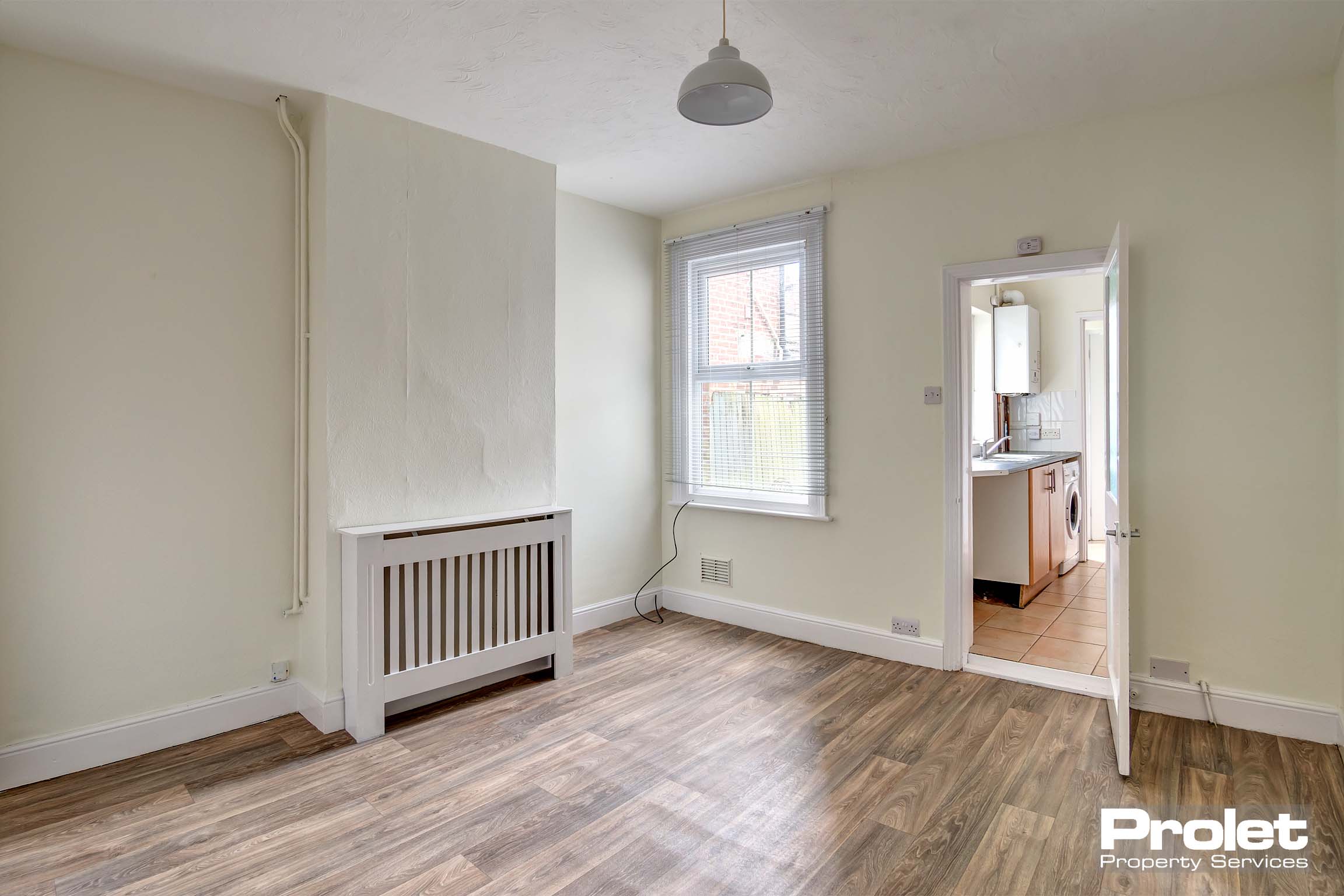 Dining room with cream walls, and wood effect lino. Leads to kitchen