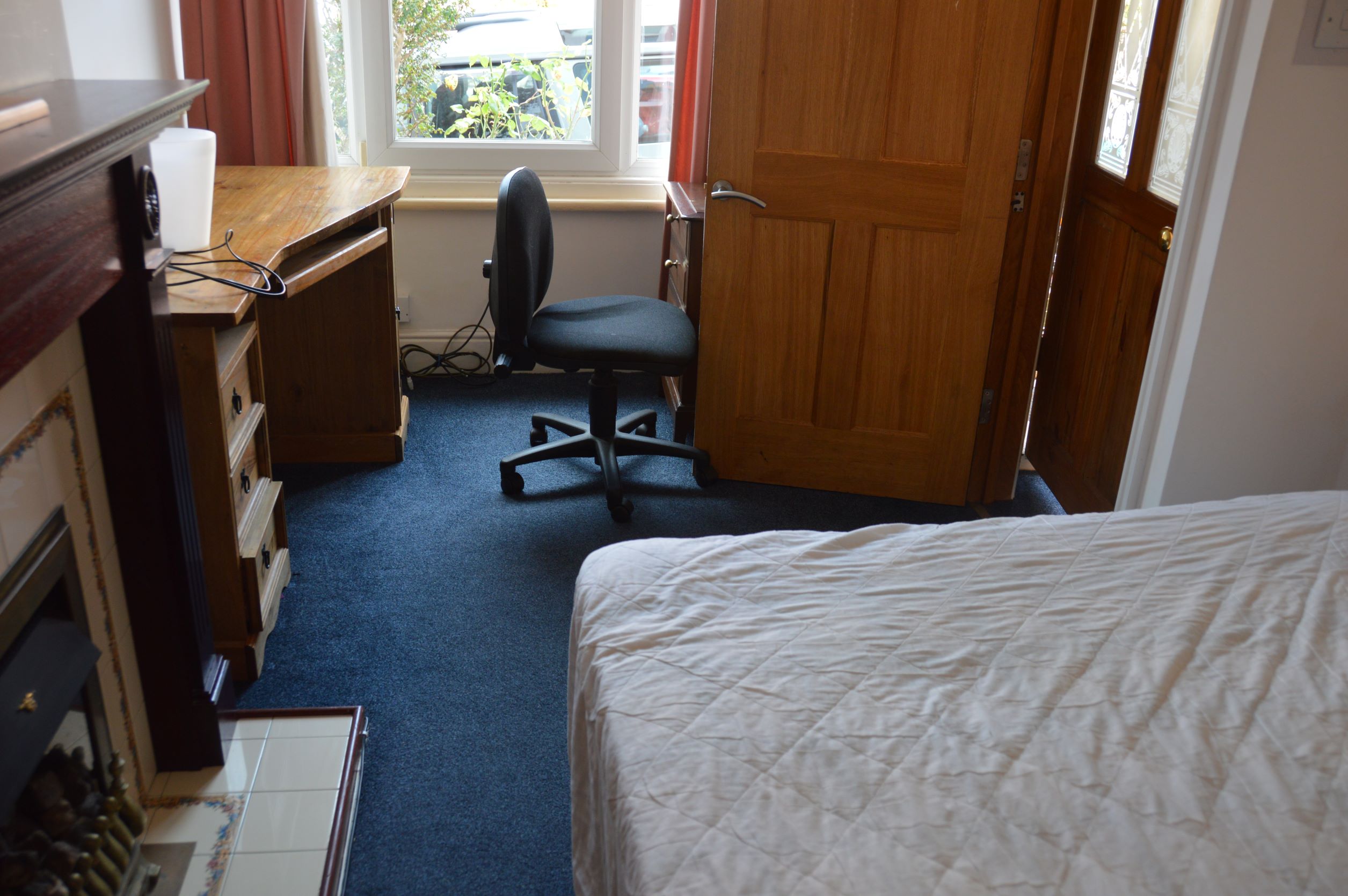 Bedroom with blue carpet, wooden desk and chair, a decorative fireplace.