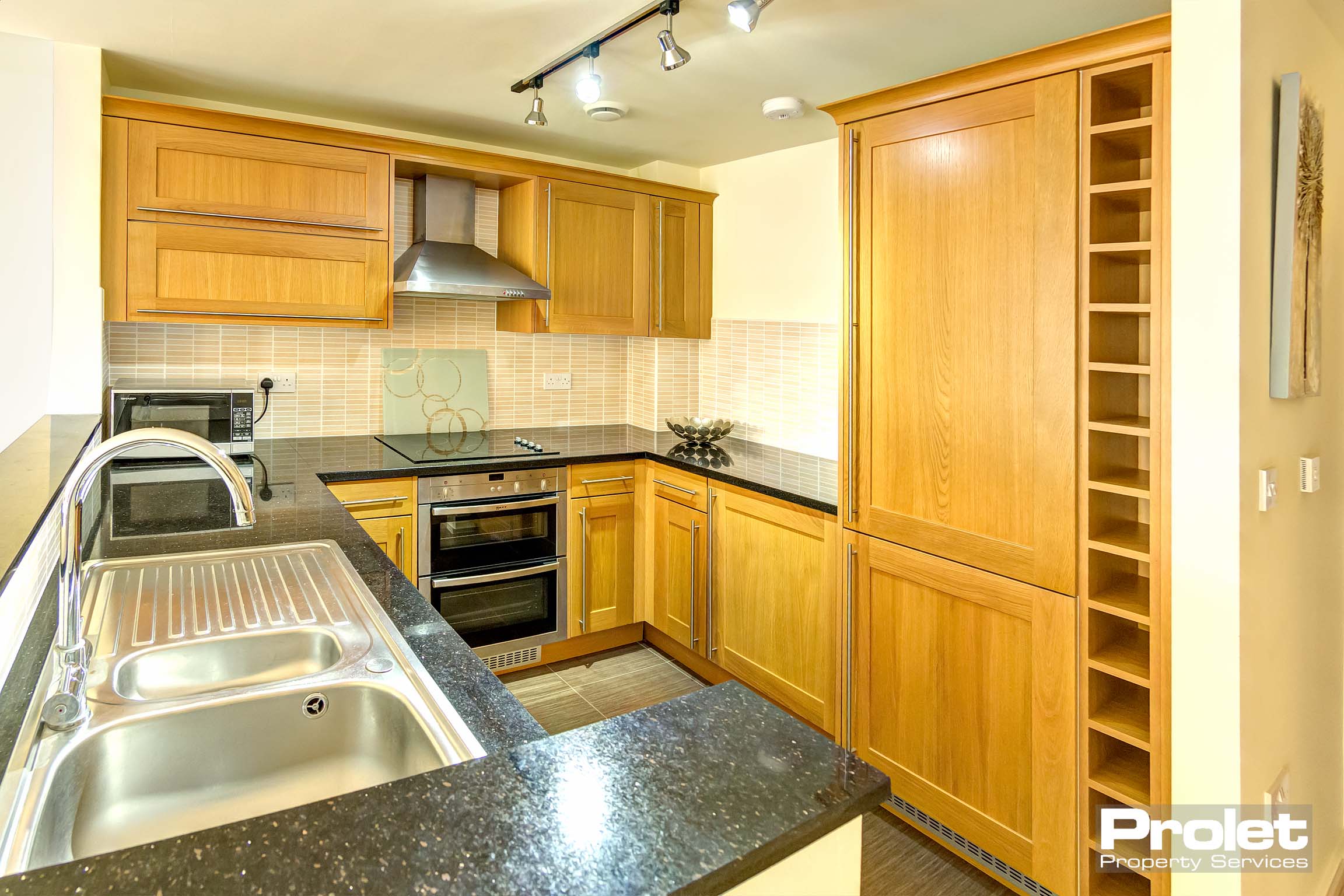 Fitted kitchen with wooden cabinets, built in oven, sink, and black worktops