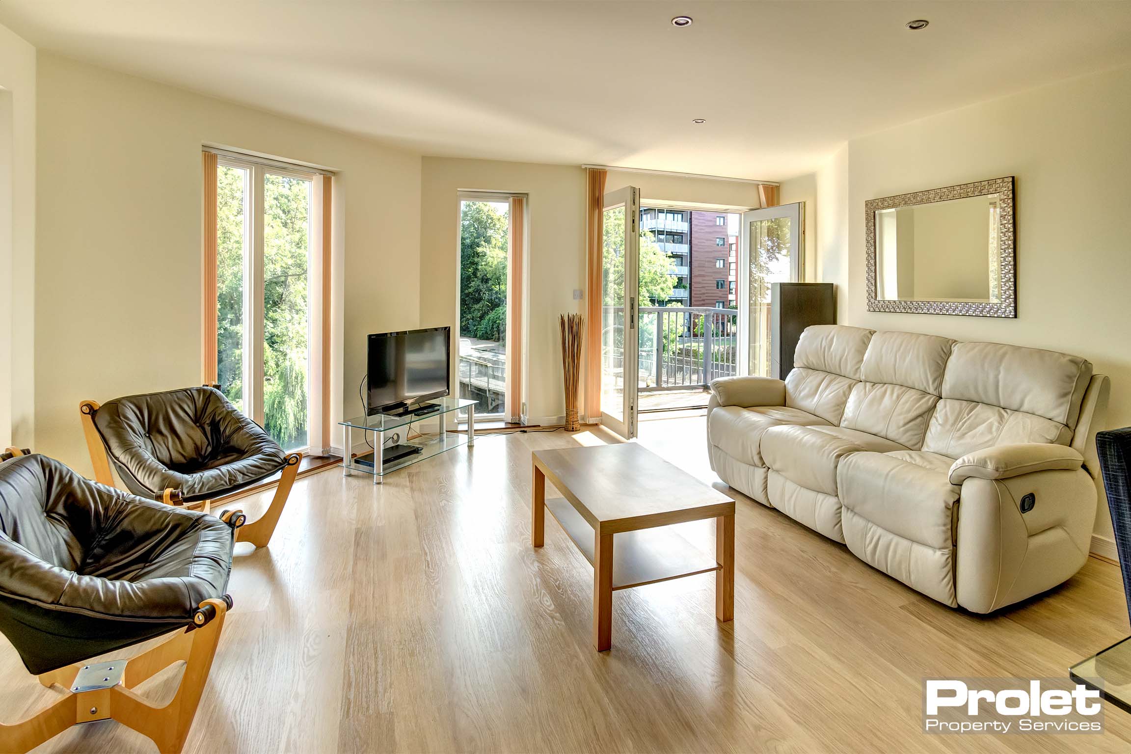 Spacious living room with wood effect laminate flooring, white sofa, black chairs, and french doors leading to balcony