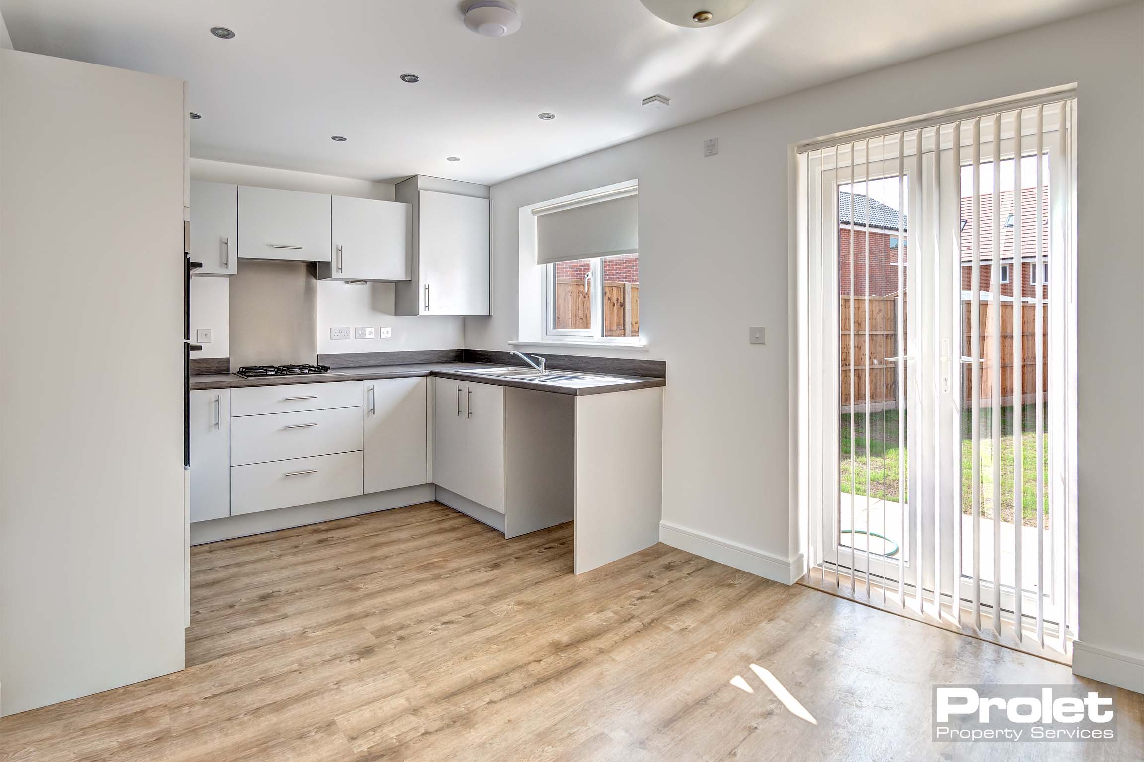 off white walls with laminate flooring. Dark worktop, hob and french doors to rear garden