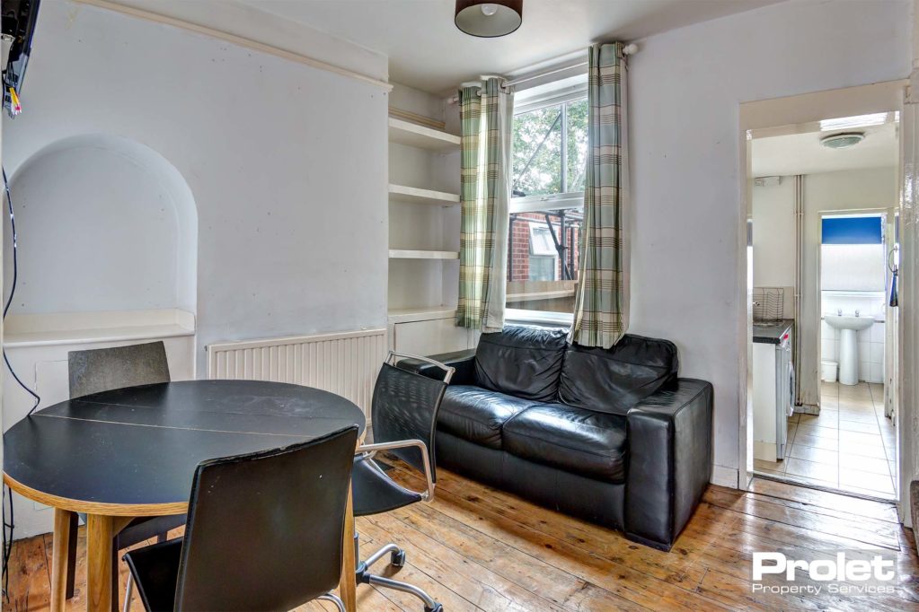Living room with wooden floor, black sofa, and round dining table and chairs.