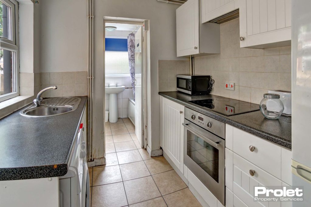 Galley kitchen with white units and black worktop