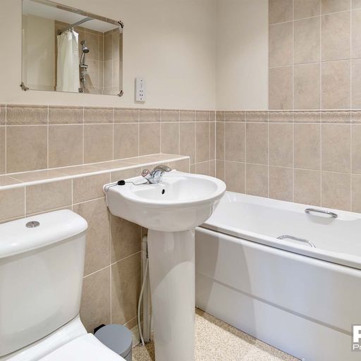 Tiled bathroom with white bath, sink and toilet.