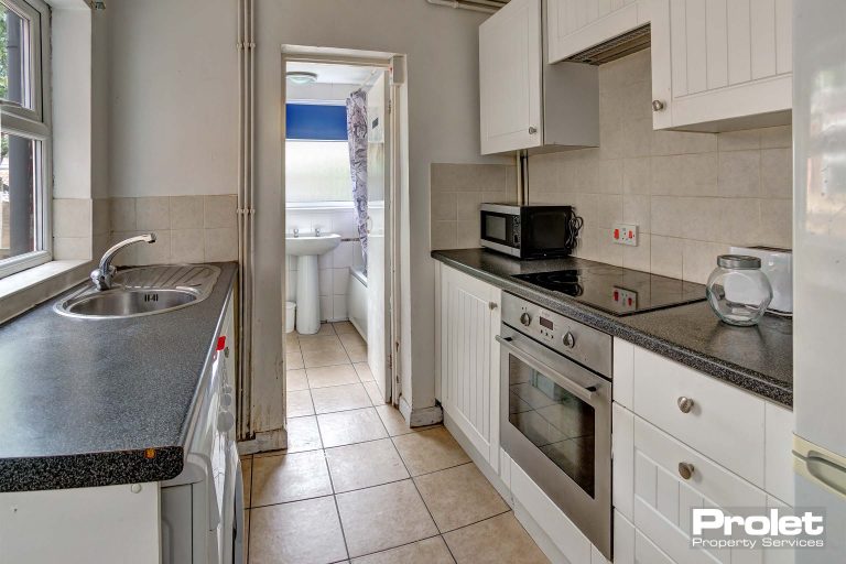 Galley kitchen with white units and black worktop