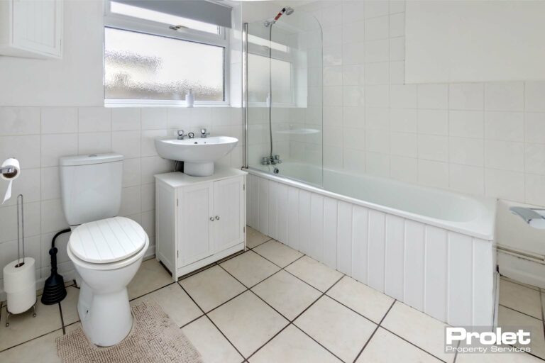 white bathroom suite with shower over bath and glass showerscreen. White walls and white floor tiles