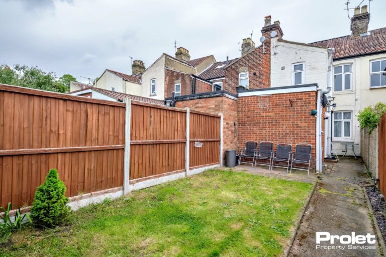 fence lined rear garden with lawn and path leading to garage