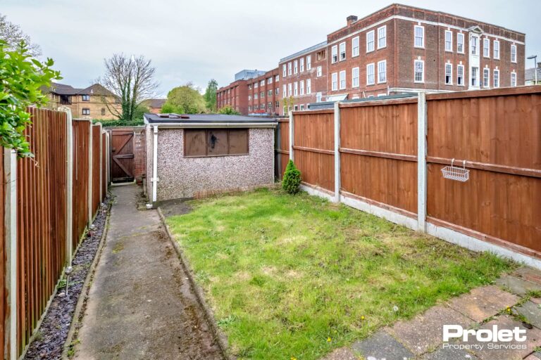 fence lined rear garden with lawn and path leading to garage