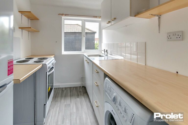 Galley kitchen with grey flooring, wood effect worktops, cabinets, and washing machine.