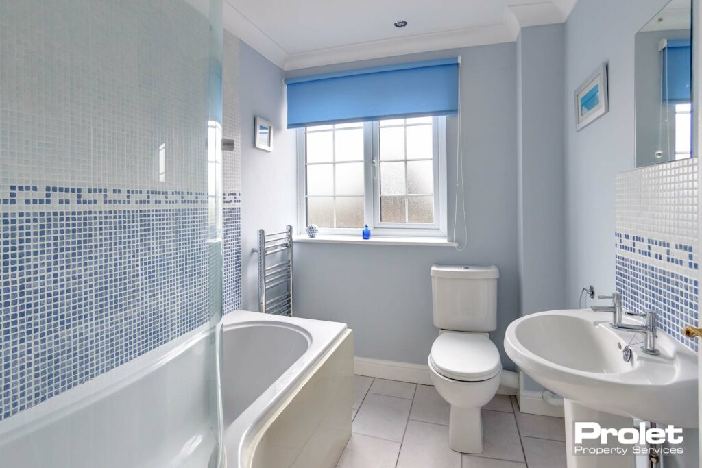 White floor tiles with blue walls. White bathroom suite with shower over bath.
