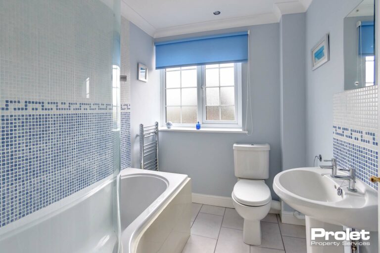 White floor tiles with blue walls. White bathroom suite with shower over bath.