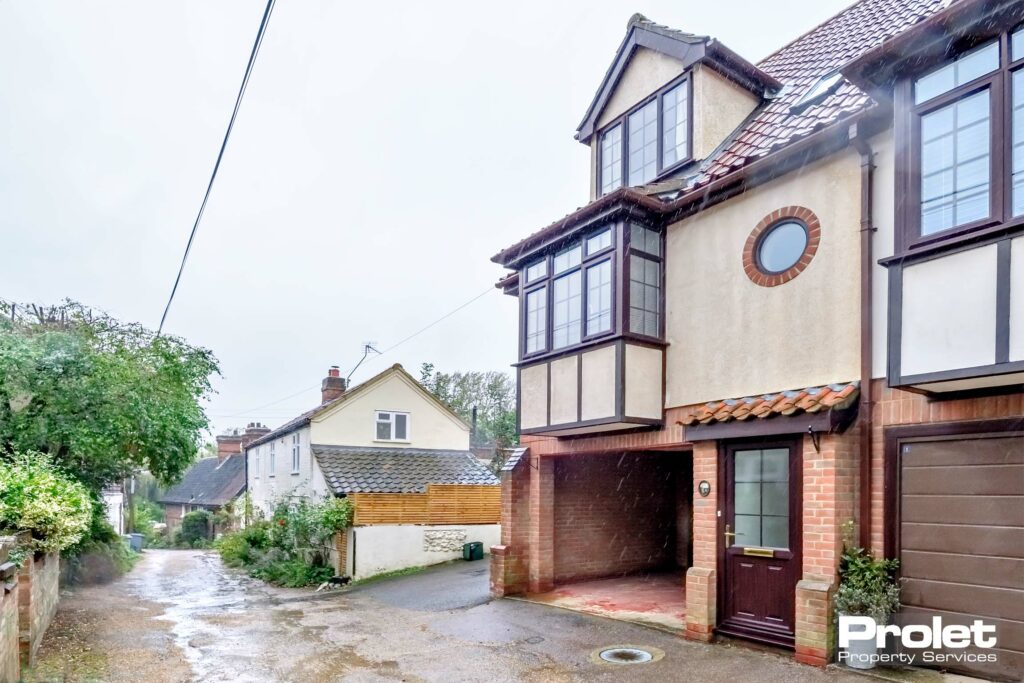 Brick building with carport leading to single garage and wooden door.