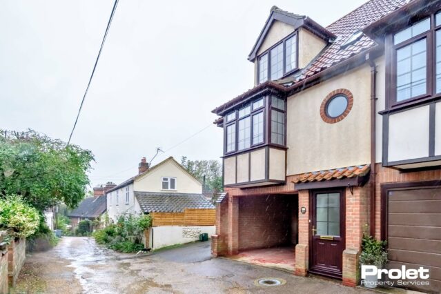 Brick building with carport leading to single garage and wooden door.