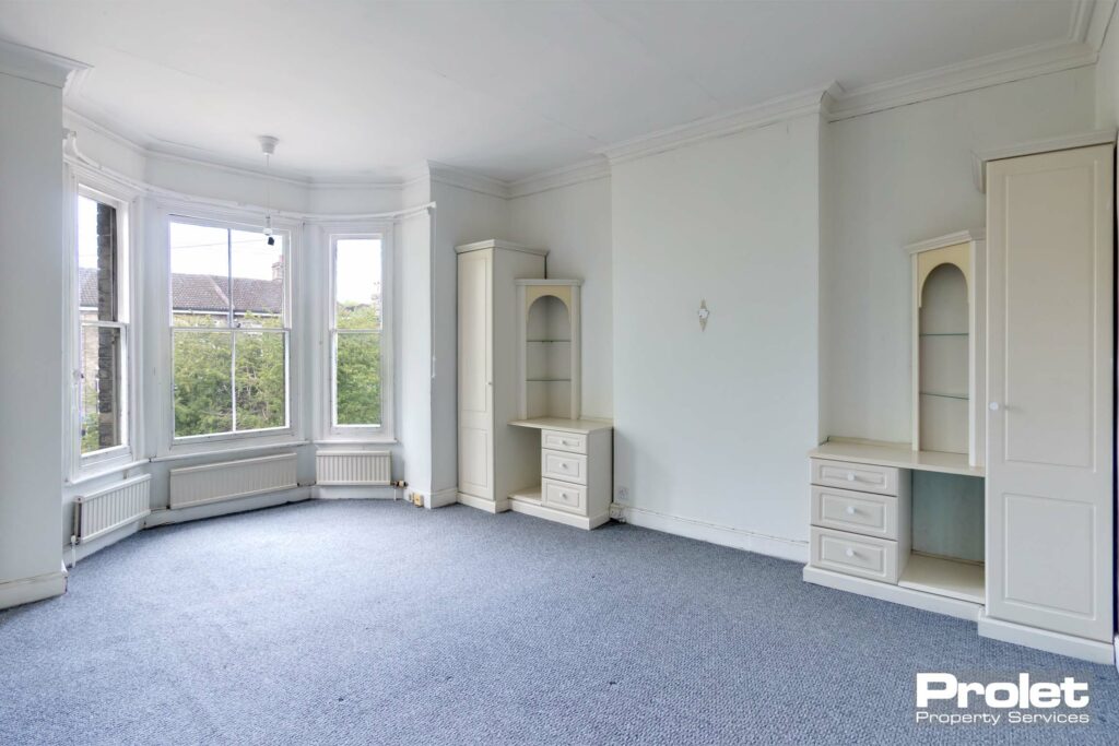 Master bedroom with grey/blue, white walls carpet and bay window. Built in wardrobes and drawers.