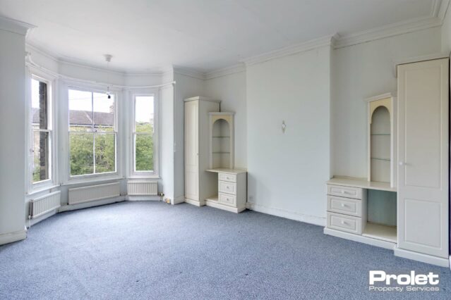 Master bedroom with grey/blue, white walls carpet and bay window. Built in wardrobes and drawers.