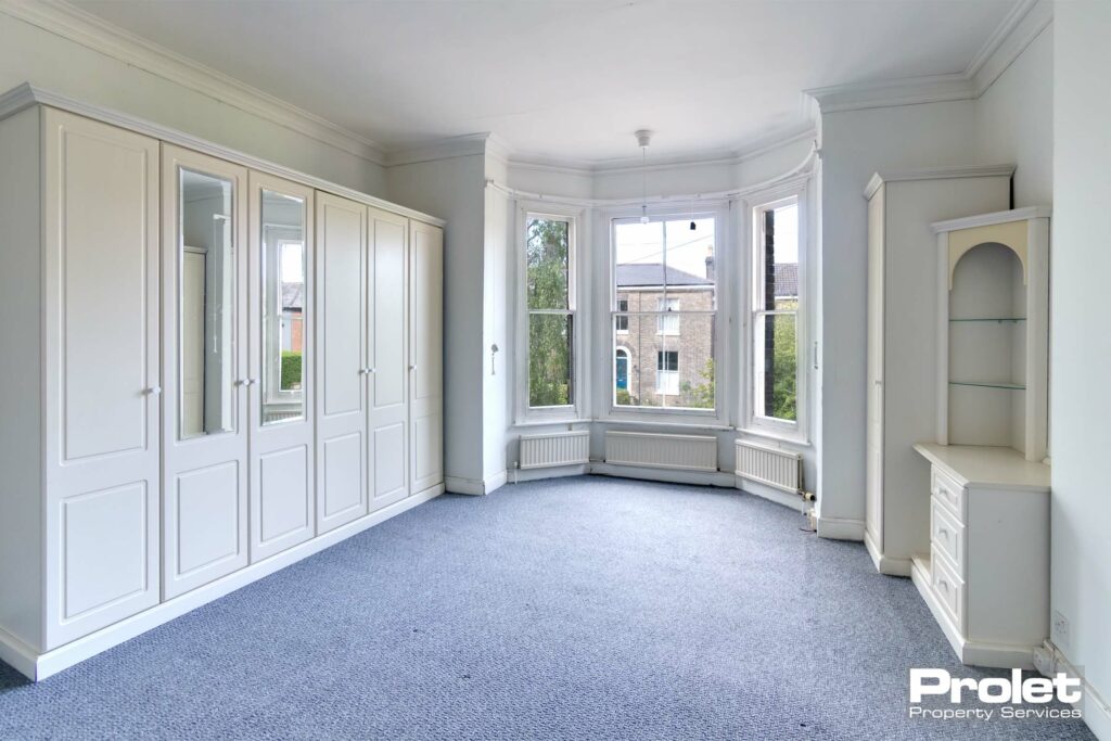Master bedroom with grey/blue carpet, white walls and bay window. Built in wardrobes and drawers.