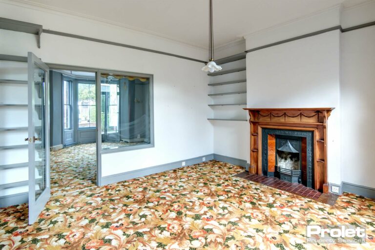 Glass pane looking through into neighbouring lounge. White walls with grey woodwork, feature fireplace and built in shelves.