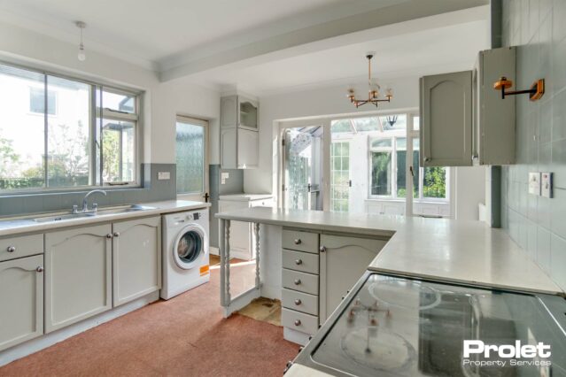 Cream worktops and units with silver handles. Peach carpet. Oven, washing machine and tumble dryer