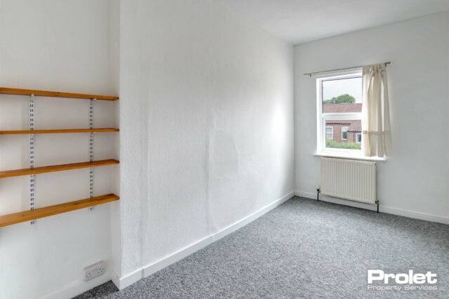 Double bedroom with grey carpet, wooden shelves, and white walls
