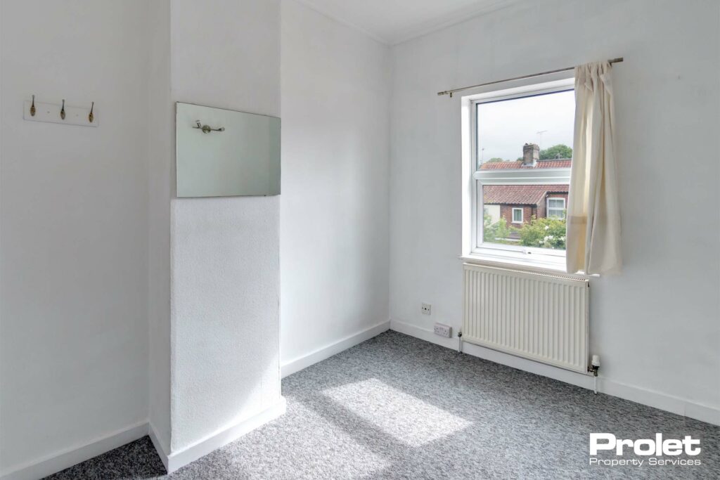 Double bedroom with mirror, coat hooks, grey carpet, and white walls