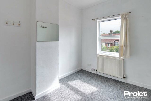 Double bedroom with mirror, coat hooks, grey carpet, and white walls