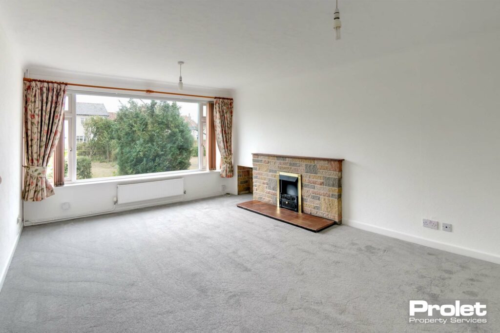 Large living room, white walls, grey carpet, and brick fireplace