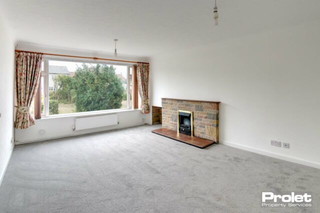 Large living room, white walls, grey carpet, and brick fireplace