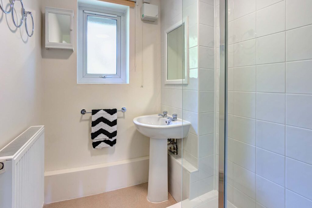 White tiles to shower cubicle with glass shower screen and white sink