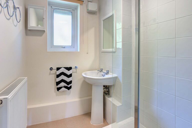 White tiles to shower cubicle with glass shower screen and white sink