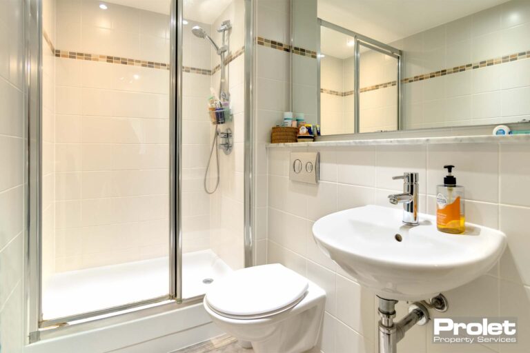 White tiles and laminate flooring with white toilet, sink and shower cubicle